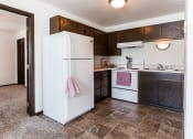 Thumbnail 5 of 8 - Grand Forks, ND Claremont Apartments. A kitchen with white appliances and dark wood cabinets.