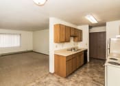 Thumbnail 7 of 10 - Grand Forks, ND Columbia West Apartments. A kitchen with white appliances and a living room with a window in the background.