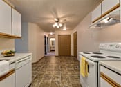 Thumbnail 8 of 28 - A kitchen with white appliances and white cabinets and a ceiling fan. Fargo, ND Eagle Run Apartments.