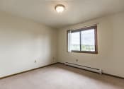 Thumbnail 11 of 14 - Bismarck, ND Eagle Sky I Apartments. A bedroom with a large window and beige carpet