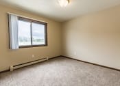 Thumbnail 7 of 14 - Bismarck, ND Eagle Sky I Apartments. A bedroom with a large window and beige carpet