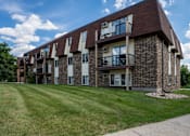 Thumbnail 19 of 21 - A brick apartment building with balconies and a green lawn in front. Bismarck, ND Belmont West Apartments