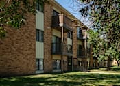 Thumbnail 9 of 9 - A brick building with balconies and trees in front. Bismarck, ND Garden Grove Apartments