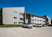 Thumbnail 8 of 8 - A grey building with a parking lot in front of it. Bismarck, ND Bradbury Apartments