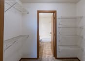 Thumbnail 10 of 13 - an empty closet with empty shelves and an open door to a bathroom. Fargo, ND Auburn II Apartments