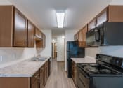 Thumbnail 6 of 17 - Fargo, ND Cambridge Apartments. A kitchen with wood cabinets and a black stove top oven