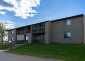 Thumbnail 1 of 6 - an exterior view of a brick apartment building with green grass