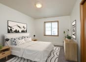 Thumbnail 4 of 18 - Fargo, ND Flickertail Apartments. a bedroom with a white bed and a wooden dresser with a plant on it
