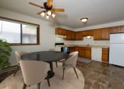 Thumbnail 4 of 9 - Fargo, ND Gemstone Apartments. a dining area with a table and chairs and a kitchen with a refrigerator and dishwasher. A window fills the room with bright natural light