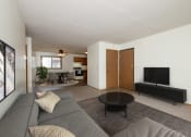 Thumbnail 3 of 9 - Fargo, ND Gemstone Apartments. A living room with a gray couch and a black coffee table. The dining room is in the background with a 4 chair table.