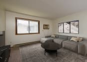 Thumbnail 2 of 9 - Fargo, ND Gemstone Apartments. A living room with a gray couch and a black coffee table. A window fills the room with bright natural light.
