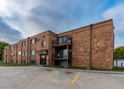 Thumbnail 13 of 13 - a brick apartment building with a parking lot and a cloudy sky. Fargo, ND Hartford Apartments