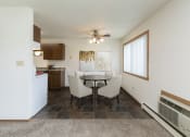 Thumbnail 2 of 34 - Fargo, ND Islander Apartments. A dining area with a four chair table that has a cailing fan with a light above it. A window brightens the room with natural light. Theres also a kitchen in the background