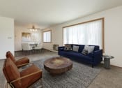 Thumbnail 1 of 34 - Fargo, ND Islander Apartments. A living room with a blue couch and leather chairs. A large window brightens the room with natural light.