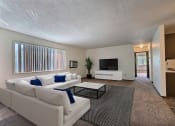 Thumbnail 1 of 18 - Fargo, ND Kingswood Apartments. A living room with a large white couch and a coffee table. A long window brightens the room with natural light