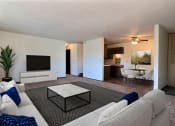 Thumbnail 2 of 18 - Fargo, ND Kingswood Apartments. A living room with a large white couch, a coffee table, and a tv. The dining room is in the background with a 4 chair table