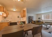 Thumbnail 5 of 18 - Fargo, ND Kingswood Apartments. A kitchen and living room with a wooden table and four chairs. The kitchen is in the background.