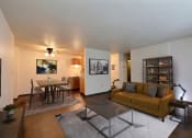 Thumbnail 4 of 18 - Fargo, ND Kingswood Apartments.  A living room with a dining room and kitchen in the background. The living room has a couch, coffee table, and a large bookshelf behind the couch