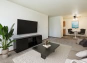 Thumbnail 3 of 20 - a living room with a coffee table and tv with a dining room in the background. Fargo, ND Maplewood Bend Apartments