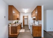 Thumbnail 10 of 20 - an open kitchen with wood cabinets and white appliances and a hallway with a door to. Fargo, ND Martha Alice Apartments