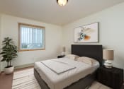 Thumbnail 3 of 17 - a bedroom with a bed and a potted plant and a window. Fargo, ND Maybrook Apartments