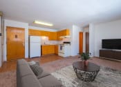 Thumbnail 4 of 15 - Fargo, ND Morningside Apartments. A living room with a couch and a coffee table. Theres a small kitchen in the background with white appliances.