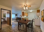 Thumbnail 4 of 21 - Fargo, ND Prairiewood Courts Apartments. A dining room and living room with a wooden table and four chairs and a ceiling fan. the living room is in the background.