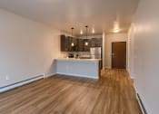 Thumbnail 13 of 26 - an empty living room with a kitchen with a sink and a refrigerator. Fargo, ND Prairiewood Meadows | LivingFargo, ND Prairiewood Meadows