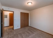 Thumbnail 13 of 22 - an empty living room with carpet and a door to a bedroom. Fargo, ND Sargent Apartments
