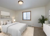 Thumbnail 5 of 10 - Fargo, ND Sugar plum apartments. A bedroom with a large white bed, white dresser, and white night stands with a lamp on each,  and window.