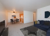 Thumbnail 2 of 10 - Fargo, ND Sugar Plum Apartments. A living room with a navy blue couch, a coffee table, and a dining area with a table and four chairs in the background.