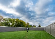 Thumbnail 2 of 2 - Fargo, ND Summerfield Apartments. A backyard with a fence and a dog in the grass