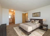 Thumbnail 4 of 9 - Fargo, ND Windgate Apartments. a master bedroom with a large bed and dresser. A bathroom is in the background