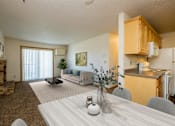 Thumbnail 3 of 9 - Fargo, ND Windgate Apartments. a dining room with a living room in the background. the dining room table has four chairs. the living room has a couch, coffee table, and a glass sliding door.