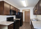Thumbnail 31 of 42 - a kitchen with black appliances and marble counter tops and dark wood cabinets. Fargo, ND Country Club Apartments