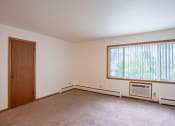 Thumbnail 5 of 18 - an empty living room with a large window and a door. Fargo, ND Crown Court 1 Apartments