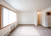 Thumbnail 12 of 18 - an empty living room with a large window and a refrigerator. Fargo, ND Crown Court 1 Apartments