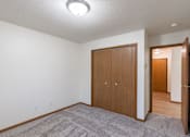 Thumbnail 17 of 23 - a living room with carpet and a door to a hallway with a closet. Fargo, ND Flagstone Apartments