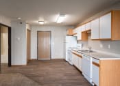 Thumbnail 14 of 16 - an empty kitchen with white appliances and wood flooring and a door to the bathroom