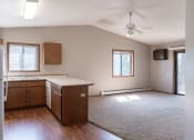 Thumbnail 9 of 19 - an empty living room with a kitchen and a ceiling fan. Fargo, ND Rosegate Apartments
