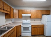 Thumbnail 10 of 25 - an empty kitchen with white appliances and wooden cabinets. Fargo, ND Westview Towers Apartments
