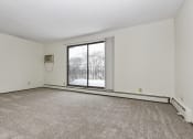 Thumbnail 6 of 32 - Fridley, MN Georgetown Apartment. A living room with a large window and a carpeted floor