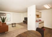 Thumbnail 5 of 19 - Grand Forks, ND Bristol Park Apartments. a living room with a couch a table and a chair and a kitchen with a sink and