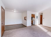 Thumbnail 9 of 14 - an empty living room with white walls and carpet and a kitchen. Grand Forks, ND Cedarwood Apartments