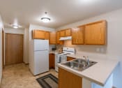 Thumbnail 12 of 17 - Grand Forks, ND Creekside Apartments. A kitchen with white appliances and wooden cabinets and a sink