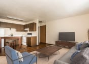 Thumbnail 4 of 23 - Grand Forks, ND Riverwood Apartments. A living room with a couch, chair, coffee table, and tv with the kitchen in the background.
