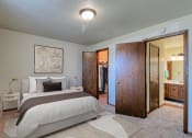 Thumbnail 7 of 19 - Grand Forks, ND Roughrider Apartments. a bedroom with a large bed and a bathroom in the background