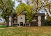 Thumbnail 1 of 6 - Grand Forks, ND Roughrider Apartments. The exterior of  a three level apartment building with a sidewalk leading to the front door.