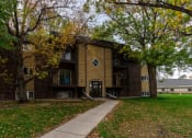 Thumbnail 1 of 19 - Grand Forks, ND Roughrider Apartments. The exterior of  a three level apartment building with a sidewalk leading to the front door.