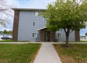 Thumbnail 21 of 22 - Grand Forks, ND Southview III Apartments. The front of a blue building with a sidewalk and a tree